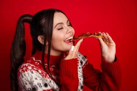 A smiling woman in festive red sweater enjoys food against red background creating a cheerful holiday vibe suitable for Christmas stock photographyの写真素材