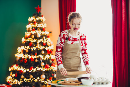 Cheerful home scene a woman in Christmas sweater baking by a decorated Christmas tree during the holiday seasonの写真素材