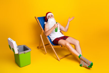 Santa Claus relaxes at home in colorful pajama sitting in a rocking chair on a bright yellow backgroundの写真素材