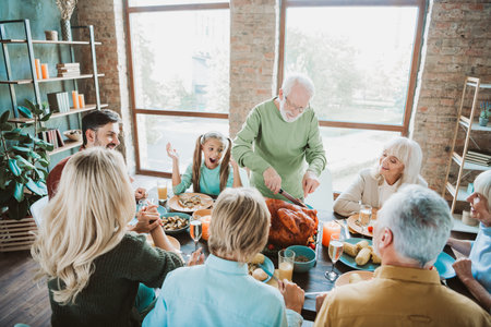 A warm family Thanksgiving gathering around a table sharing a roasted turkey joy laughter and gratitude in a bright cozy home settingの写真素材