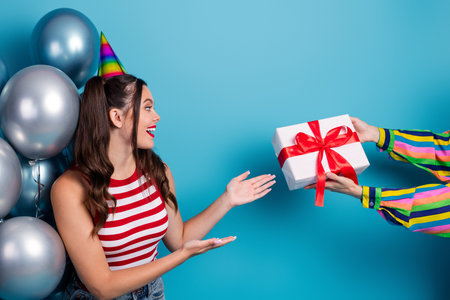 Cheerful young woman in casual attire receiving a gift box with a red bow during a festive celebrationの写真素材