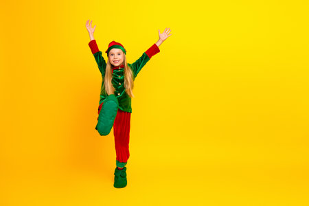 Cheerful child dressed as a festive elf posing joyfully on a vibrant yellow background, celebrating Christmas with charmの写真素材