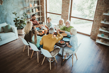 Funny warm family feast at a modern home celebrating Thanksgiving with grandparents parents children and friends around a large table enjoying food laughter and reunionの写真素材