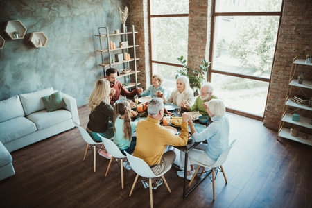 Family gathering around table for Thanksgiving dinner with friends and relatives in modern home...
