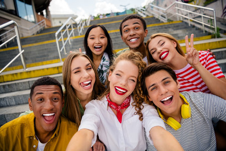 Funny young friends enjoying a cheerful moment together outdoors on urban stairs during a sunny summer dayの写真素材