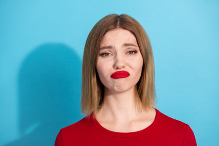 Young woman in a red shirt posing against a bright blue background, expressing emotions with a...