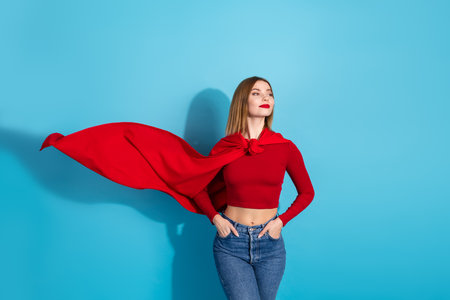 Adorable young woman in trendy red attire poses confidently against a vibrant blue backdropの写真素材