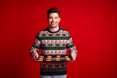 Playful man in a christmas sweater proudly presents a tray of cookies spreading holiday joy and festive cheer for xmas shoppersの写真素材