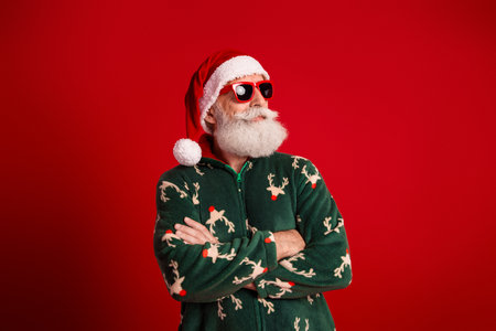 Santa in a festive green sweater with red hat and sunglasses strikes a confident pose against a bold red backgroundの写真素材