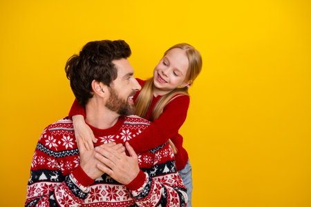 Cheerful father and daughter in festive sweaters sharing joyful moments against a bright yellow backgroundの写真素材