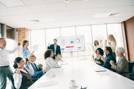 Diverse professional team celebrates success during an office presentation showcasing teamwork and collaboration in a modern workplaceの写真素材