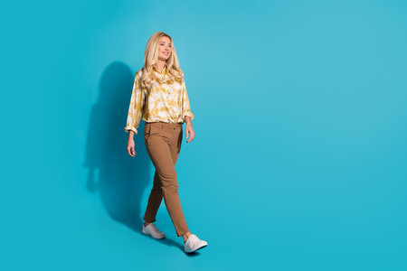 Full length photo of attractive mature woman walking dressed in stylish formalwear clothes isolated on cyan color backgroundの写真素材