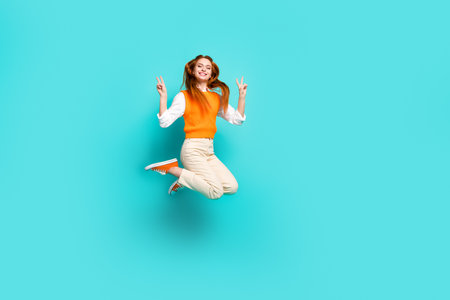 Photo of cheerful lovely funny girl wear orange trendy clothes jump up hands v-sign isolated on...