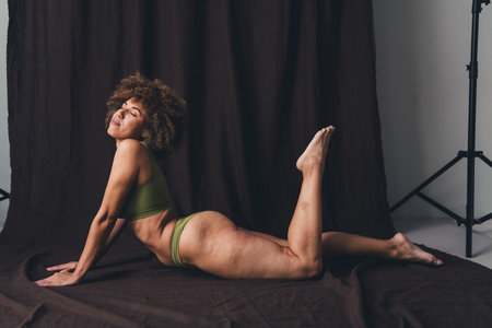 Full size photo of young lady lying posing on the floor dressed in khaki lingerie with a studio background, emphasizing self-acceptance and natural beauty.の写真素材