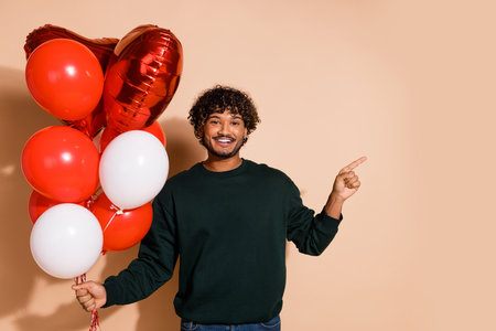 Photo of good mood guy wear sweatshirt rising balloons showing emtpy space isolated beige color backgroundの写真素材