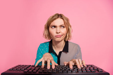 Photo of pretty girl unsure web camera typing keyboard look empty space wear trendy striped cyan outfit isolated on pink color backgroundの写真素材
