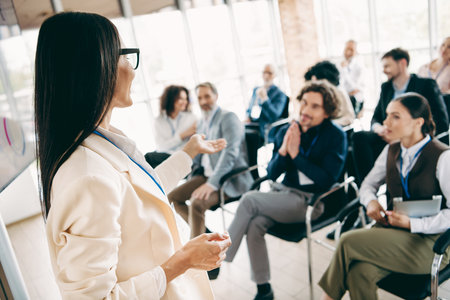 Female Presenter Engaging with a Professional Audience During an Office Training Session, Highlighting Collaboration and Teamworkの写真素材