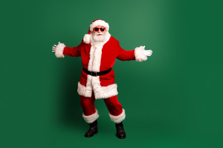 Funny Santa in red suit stands with arms wide on green background ready for Christmas celebrations