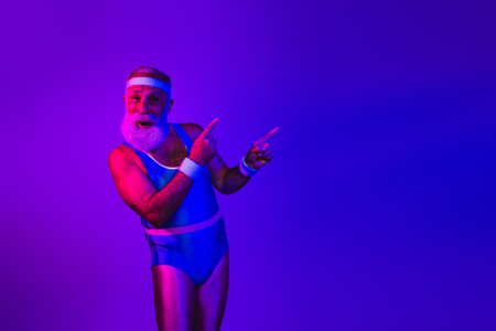 Senior male in retro blue jumpsuit dances under neon purple blue lights with joyful athletic energyの写真素材