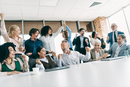 Diverse group of business professionals celebrating success with excitement during a team meeting in a modern officeの写真素材