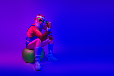 Retro fitness icon sits on a stability ball under neon purple blue lights holding a dumbbellの写真素材