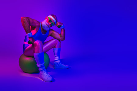 Retro fitness icon relaxes on a stability ball under neon violet and blue lights in a bold colorful workout vibeの写真素材