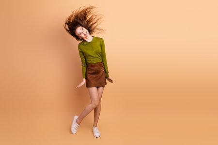 Young woman model dancing against beige background wearing olive green top and brown skirt with joyful energy and casual stylish fashion lifestyleの写真素材