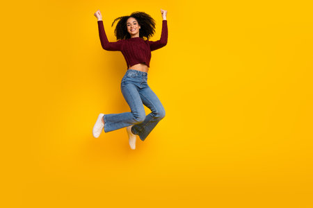 Young female mixed race model leaps with joy against a bright yellow background conveying energy...