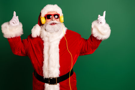 Santa in red suit with yellow headphones dances against a green backdrop for Christmas fun and holiday energyの写真素材