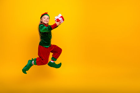 Festive Elf in Green and Red Jumps Joyfully on Yellow Background with Holiday Gift Boxの写真素材