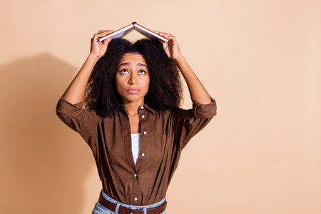 Photo of funky adorable girl with perming coiffure wear brown blouse holding book like roof on head isolated on pastel color backgroundの写真素材