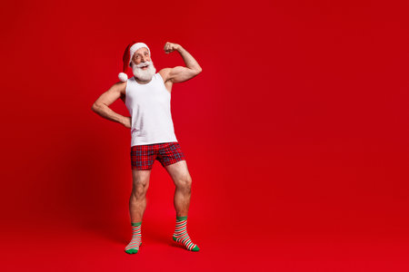 Santa flexes in festive red studio wearing hat and plaid shorts for a Christmas themed stock photoの写真素材