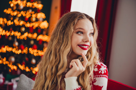 Funny holiday moment a cheerful blonde woman in a red sweater smiles beside a twinkling christmas tree at homeの写真素材