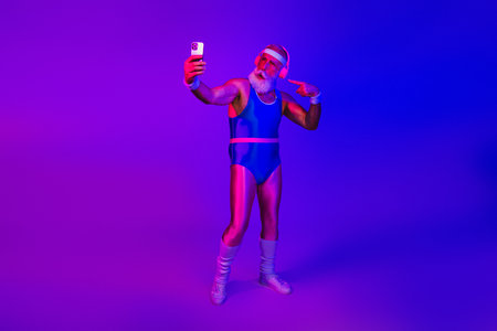 Senior male fitness icon in retro jumpsuit takes a neon blue selfie and celebrates joy style and wellness in a vibrant studioの写真素材