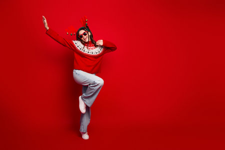 Joyful woman in red christmas sweater dances against a bold red background creating a festive holiday vibe for a seasonal stock photoの写真素材