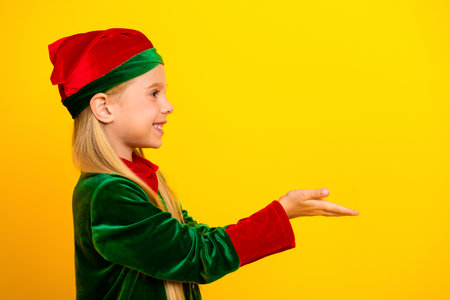 Smiling child in a festive elf costume poses against a vibrant yellow background, ready to spread Christmas cheer and joyの写真素材