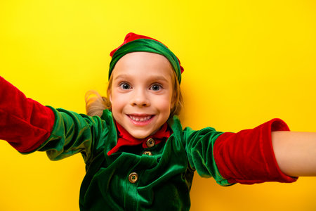 Joyful little girl dressed as an elf with a vibrant yellow background, spreading festive cheer during the holiday seasonの写真素材