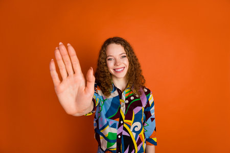 Photo of adorable positive cute girl wear stylish print clothes showing palm hand isolated on vivid orange color backgroundの写真素材