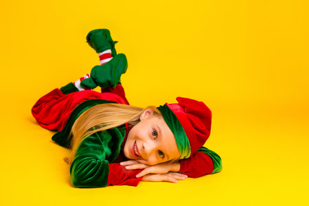 Festive child dressed in a Christmas elf costume smiling on a bright yellow background, perfect for holiday themesの写真素材