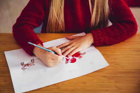 Creative kid in red sweater sketches festive holiday scene at cozy home desk for merry Christmas joyの写真素材