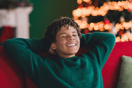 Happy teenage boy relaxing on a festive sofa during Christmas time, surrounded by sparkling decorations and cozy atmosphereの写真素材