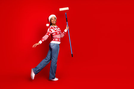 Funny santa girl in red sweater paints holiday joy with a rolling fun on a bright winter red backgroundの写真素材