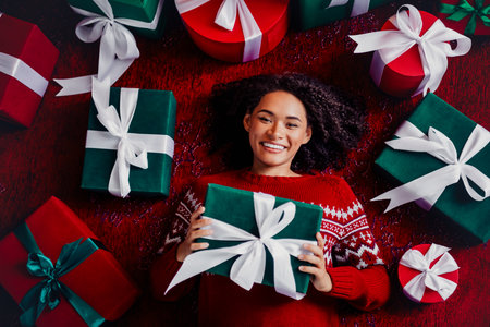 Fun holiday scene with a smiling woman in a red sweater surrounded by gifts and decorations in a...