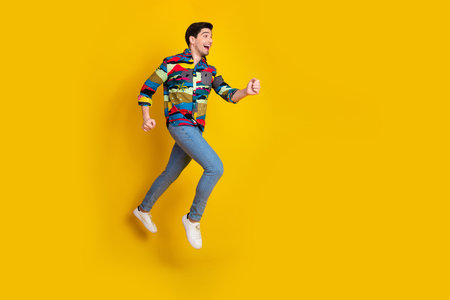 Young man in colorful print shirt jumps with joy against a bold yellow background conveying energy...