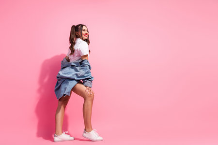 Young woman in casual summer fashion smiles against pink background wearing a white top with denim jacket and white sneakersの写真素材