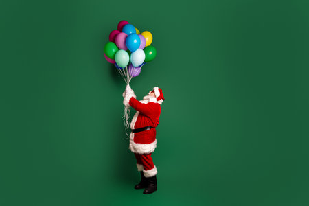 Santa holds colorful balloons against a green background for a festive Christmas scene perfect for holiday season celebration and family funの写真素材