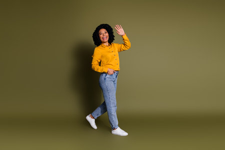 Full size profile photo of pretty lady walk arm wave hi wear yellow shirt isolated on khaki color backgroundの写真素材