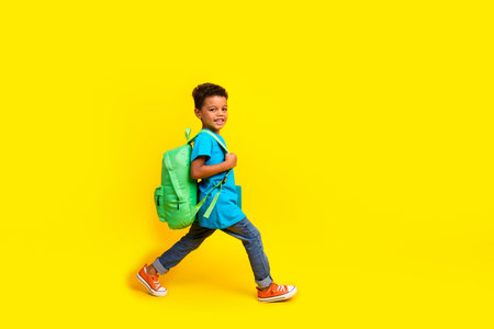Full body photo of diligent funky small child dressed blue t-shirt jeans hold bag go empty space isolated on vibrant yellow backgroundの写真素材