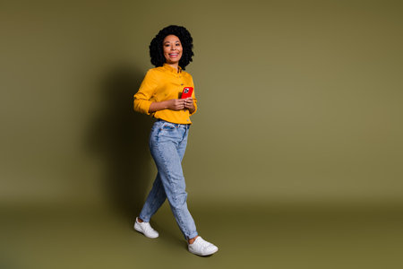Full size photo of nice young woman hold smart phone walk wear yellow shirt isolated on khaki color backgroundの写真素材