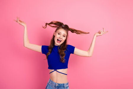 Playful young woman with vibrant hairstyle smiling expressively against a pink background in a trendy blue topの写真素材